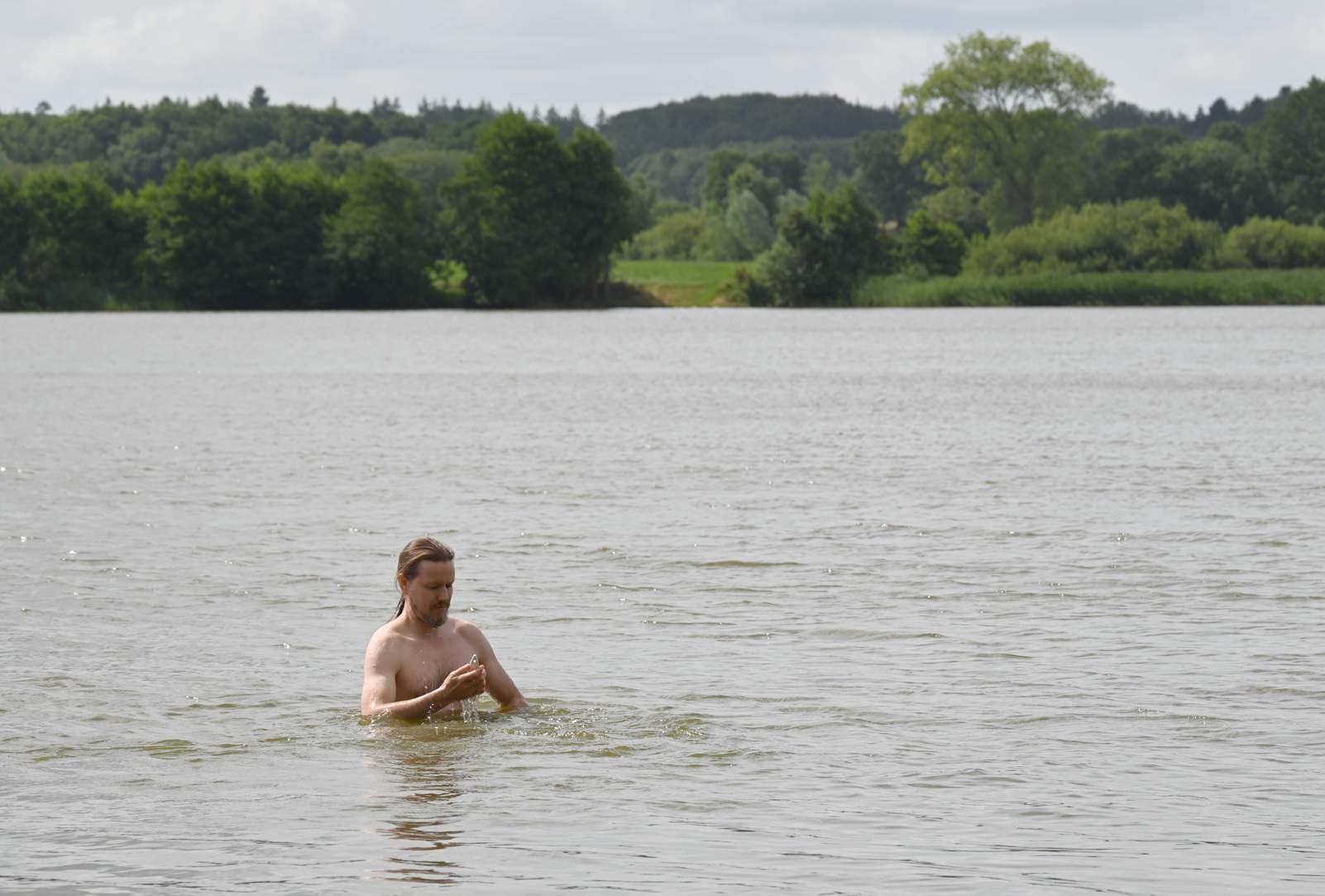 Ein Mann steht bis zur Brust im Wasser eines Sees und wirft einen Blick auf ein Thermometer.